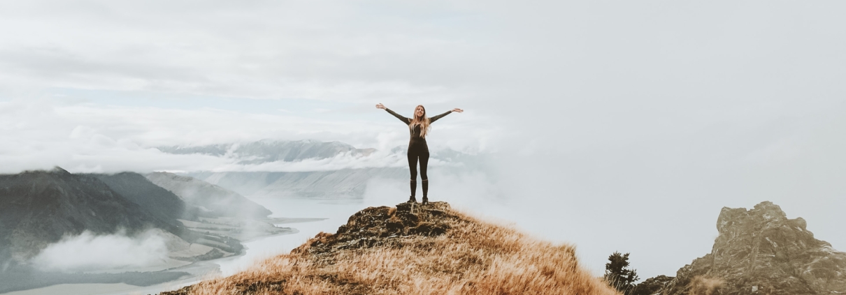 strong woman standing on mountain with arms in the air